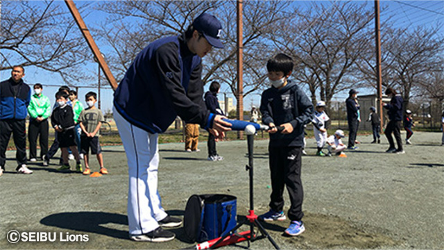 選手が少年にバットへのボールの当て方を指導している様子