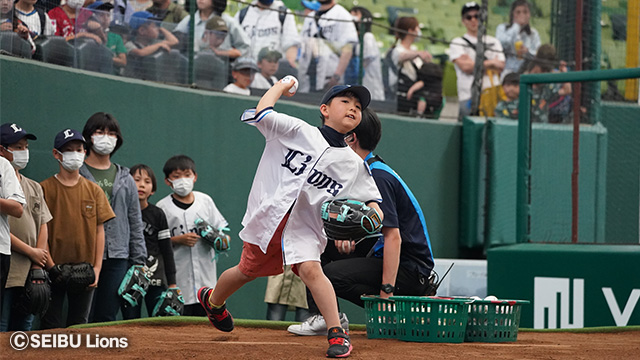 球場で胸にLionsと書かれた半袖のユニフォームを着てボールを投げる少年